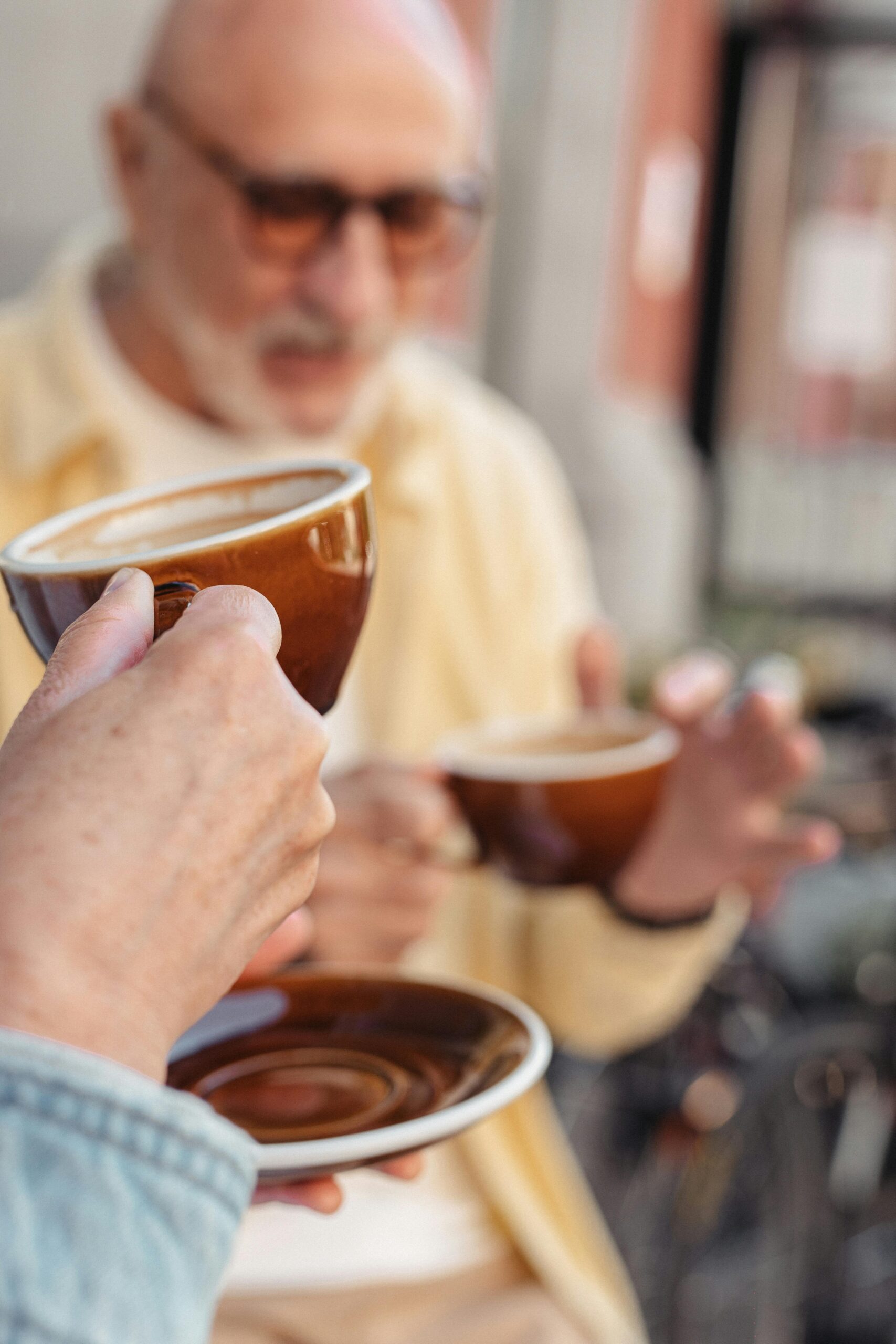 Two senior adults savor coffee, holding mugs, in a warm social setting.